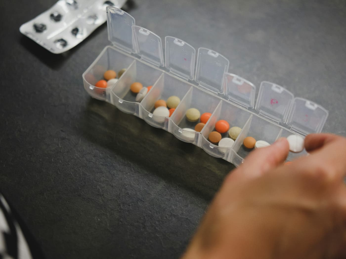 A weekly unit-dose organiser being filled, one compartment at a time
